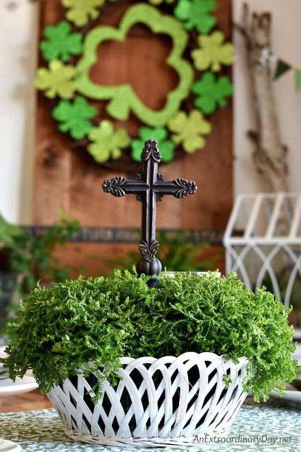 Simple centerpiece with a white basket filled with trailing Irish moss and a cross for St. Patrick's Day - AnExtraordinaryDay.net