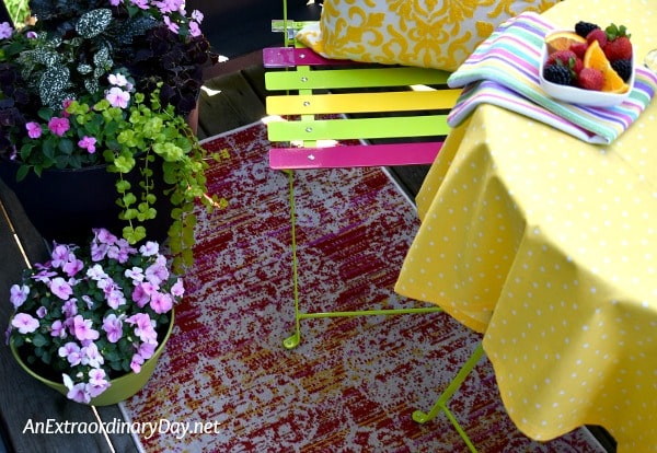 Stylish outdoor rug with shades of pink, yellow, and cream sits under a color bistro set in coordinating colors