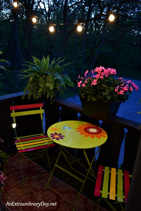 Night view of a colorful apartment balcony with bistro set illuminated with outdoor string lights